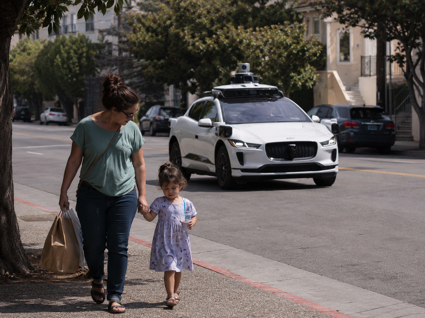 A mother and child walk unaware of a Waymo behind them